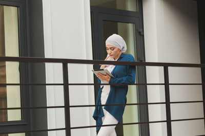 Side view of young woman standing by railing