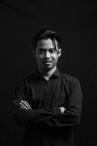 Portrait of young man standing against black background