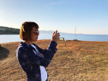 Woman photographing at beach against sky