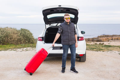 Portrait of man standing by boat on sea shore against sky