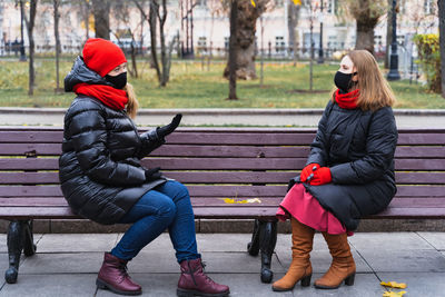 Full length of women sitting on bench in winter