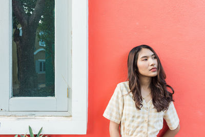 Portrait of a beautiful young woman standing against window