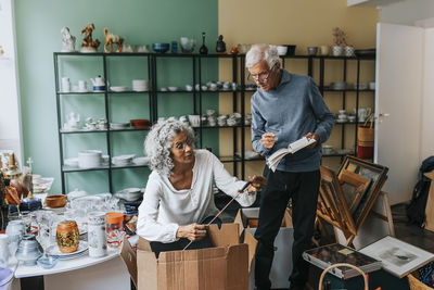 Elderly female entrepreneur analyzing fishing rod with male colleague at antique shop