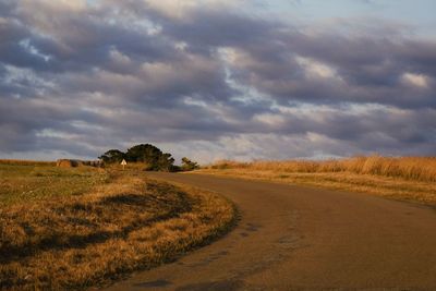 Dirt road amidst field against sky