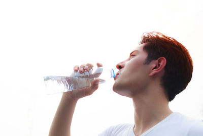 Low angle view of young man drinking water against clear sky