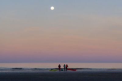 People on beach against sky during sunset