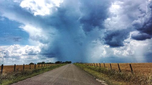 Road amidst field against storm clouds