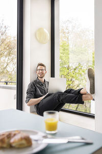 Happy man using laptop at the window at home