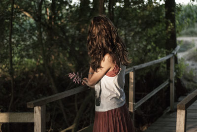 Side view of woman standing on footbridge against trees