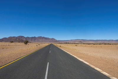 Empty road against clear blue sky