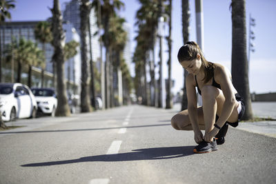 Woman tying shoelace on street in city