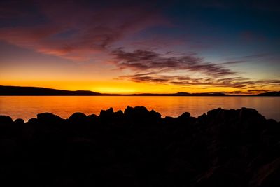 Silhouette rocks by sea against sky during sunset