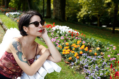 Young woman wearing sunglasses looking away while sitting on bench