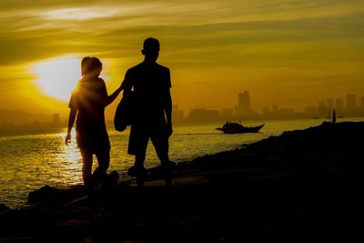 Silhouette men standing on beach against sky during sunset