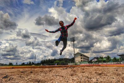 Full length of man jumping against cloudy sky