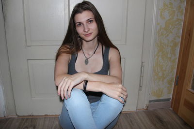 Portrait of young woman sitting on wooden door at home