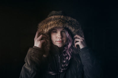 Portrait of woman wearing fur hood against black background