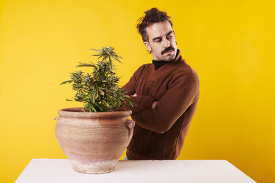 Young woman holding potted plant against yellow background