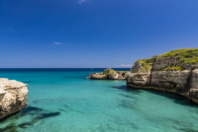 Rocks by sea against blue sky