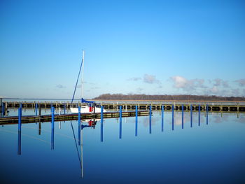 Wooden posts in lake against clear blue sky