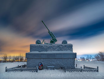 Built structure on snow covered field against sky during sunset