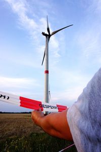 Cropped hand holding cordon tape with windmill in background against blue sky