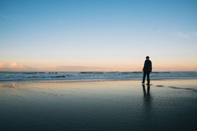 Rear view of man standing on beach during sunset