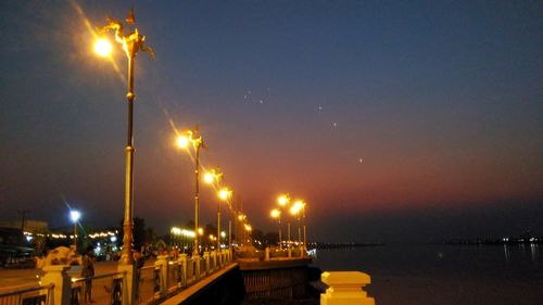 Illuminated street light by sea against sky at night