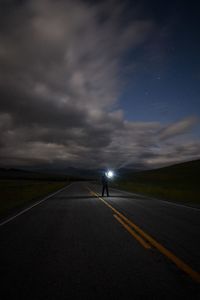 Man holding flashlight while standing on road at night