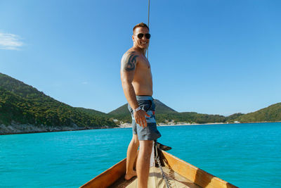 Portrait of man standing in boat on sea against sky