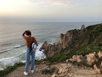 Rear view of man standing on rock by sea against sky