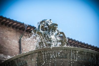 Low angle view of fountain against building against clear blue sky