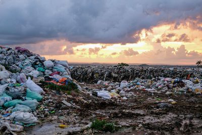 Stack of garbage on rock against sky during sunset