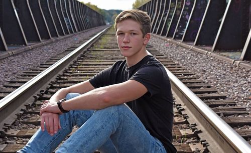 Portrait of young man sitting on railroad track