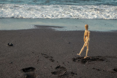 A wooden dummy walks along the beach with black sand