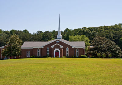 Church amidst green landscape and trees against clear blue sky