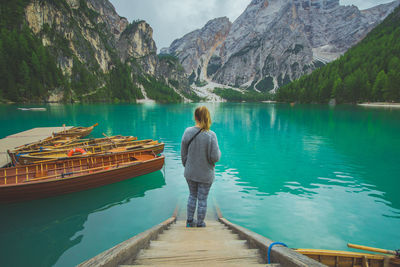 Rear view of woman standing on while looking at boats on lake against mountains