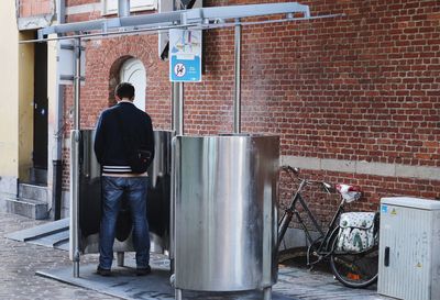 Rear view of man urinating at public restroom 