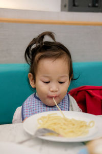 Cute girl eating spaghetti while sitting in restaurant