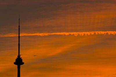 Silhouette communications tower against orange sky