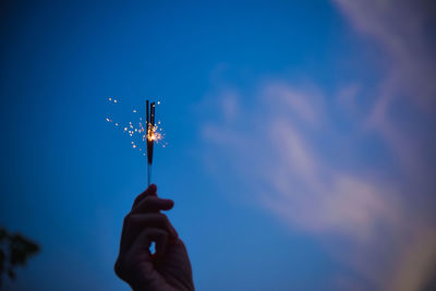 Low angle view of hand holding umbrella against blue sky