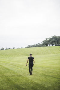 Rear view of young man walking on agricultural field against sky