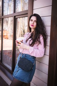 Portrait of beautiful woman with drink leaning on house wall