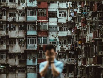 Blurred image of man covering his face standing against residential buildings in city