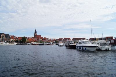 Boats in river by buildings in city against sky