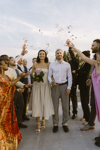 Group of male and female friends throwing confetti on newlywed couple