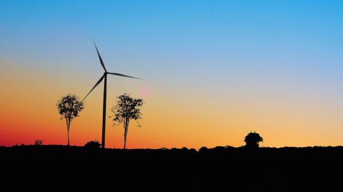 Silhouette of wind turbines on field against sky at sunset