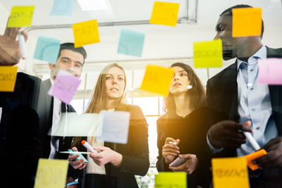 Low angle view of colleagues discussing over adhesive notes seen through glass