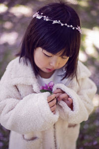 Korean girl in a white light fur coat and a headband stands in a garden with cherry blossoms