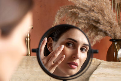 A young woman in front of a mirror applies a moisturizer on her face. beauty portrait,